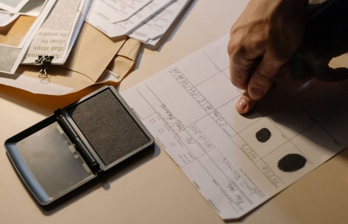 Detailed view of a hand taking fingerprints on a document with ink pad on desk.