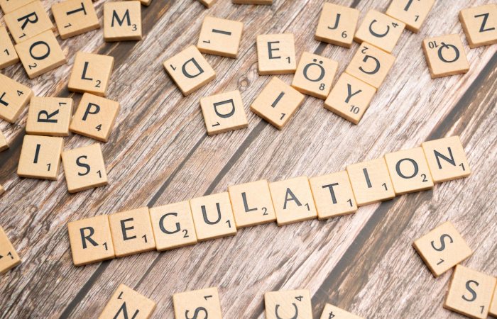 Wooden letter tiles spelling 'Regulation' on a textured wood background, conveying themes of compliance and structure.