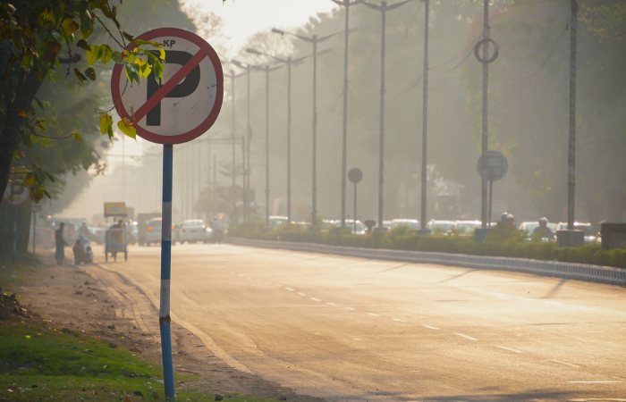 View of a bustling Indian street with a no parking sign, trees, and vehicles in the warm evening light.