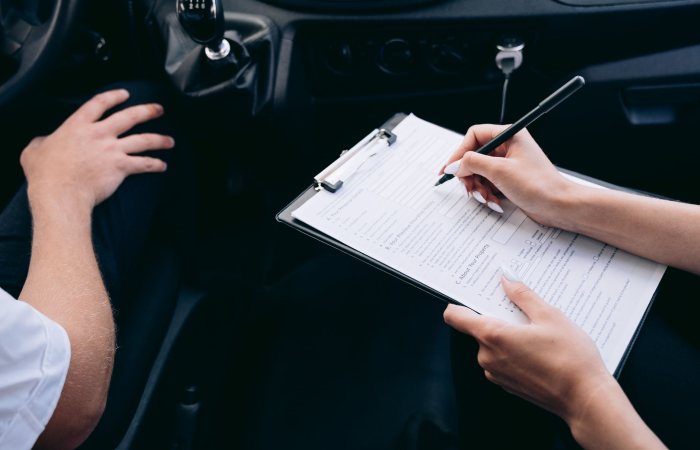 Close-up of a person writing on a clipboard inside a car, showing hands and a gear shift.